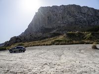 a grey car is parked by the side of a mountain in front of some rocks