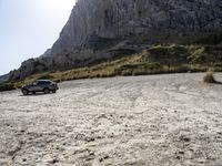 a grey car is parked by the side of a mountain in front of some rocks