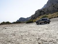 a grey car is parked by the side of a mountain in front of some rocks