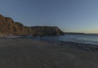 some rocks and a view of the water and a large mountain by the beach or shore