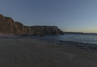 some rocks and a view of the water and a large mountain by the beach or shore