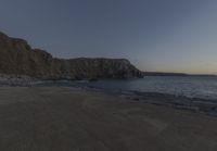 some rocks and a view of the water and a large mountain by the beach or shore