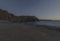 some rocks and a view of the water and a large mountain by the beach or shore