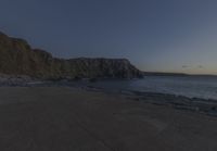 some rocks and a view of the water and a large mountain by the beach or shore