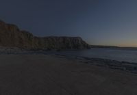 some rocks and a view of the water and a large mountain by the beach or shore