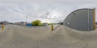 a fisheye view of an outside area with buildings and trees in the background and clouds over the sky