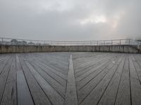 a view of a deck with a bridge in the background and a cloudy sky above