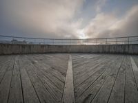 a view of a deck with a bridge in the background and a cloudy sky above