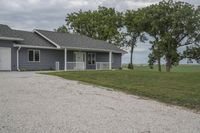 a nice grey house near the grass and trees with clouds in the background and a driveway