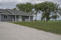 a nice grey house near the grass and trees with clouds in the background and a driveway