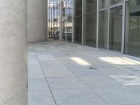 there is a gray tiled sidewalk outside the building, with large glass windows and large stone pillars