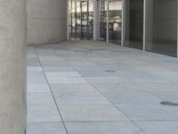 there is a gray tiled sidewalk outside the building, with large glass windows and large stone pillars