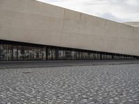 a man is standing on the sidewalk in front of an empty building on a cloudy day