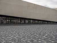 a man is standing on the sidewalk in front of an empty building on a cloudy day