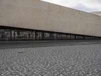 a man is standing on the sidewalk in front of an empty building on a cloudy day