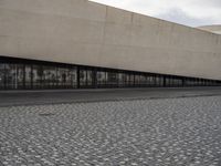 a man is standing on the sidewalk in front of an empty building on a cloudy day