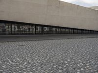 a man is standing on the sidewalk in front of an empty building on a cloudy day