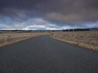 empty road leading into a field with cloudy skies above it and trees in the distance