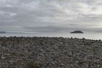 a rocky plain with boulders and water in the distance, with a cloudy sky above the ocean