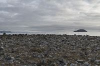 a rocky plain with boulders and water in the distance, with a cloudy sky above the ocean