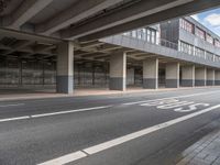 the empty street is near the big building at the intersection of the road and the side of a road