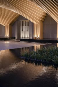 a person standing next to a pond in the center of an art building with lights on