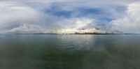 a body of water with a bridge over it, in the distance is clouds and a city on the horizon