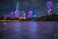 the city skyline has many purple lights on it's buildings at night time, and people in front of it