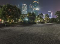 an empty, city park at night with tall buildings behind it and lights shining on the sky