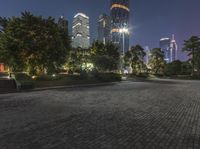 a brick road surrounded by tall buildings at night, near a garden area and a park