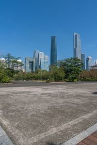 an empty parking lot in front of a skyline with high rise skyscrapers and green trees