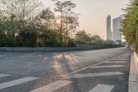 a road next to trees near a highway in a city with tall buildings behind it