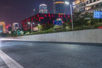 a city street with buildings and neon lights at night time in hong china as seen from an empty city highway