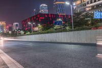 a city street with buildings and neon lights at night time in hong china as seen from an empty city highway