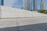 skate boarders are riding on a concrete pavement with tall buildings behind them as the person walks by