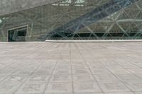 two people are walking around in front of a glass building with stairs inside the area