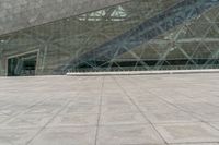 two people are walking around in front of a glass building with stairs inside the area