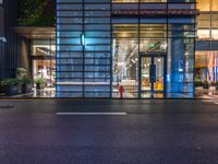 the outside of a tall glass building at night in front of it, on a street with multiple parking meters