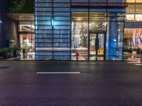 the outside of a tall glass building at night in front of it, on a street with multiple parking meters