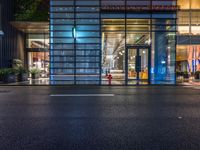 the outside of a tall glass building at night in front of it, on a street with multiple parking meters