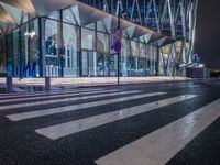 a street view of a glass building at night, in a city near a big building