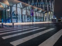 a street view of a glass building at night, in a city near a big building