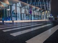 a street view of a glass building at night, in a city near a big building