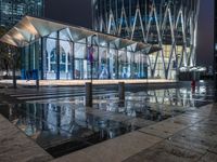 a building with a glass front sitting next to a puddle of water under the light