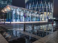 a building with a glass front sitting next to a puddle of water under the light