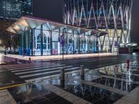 a building with a glass front sitting next to a puddle of water under the light