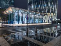 a building with a glass front sitting next to a puddle of water under the light