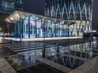 a building with a glass front sitting next to a puddle of water under the light