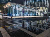 a building with a glass front sitting next to a puddle of water under the light