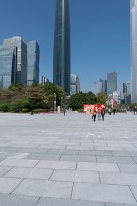 an outdoor plaza, filled with people walking around and tall buildings in the background,